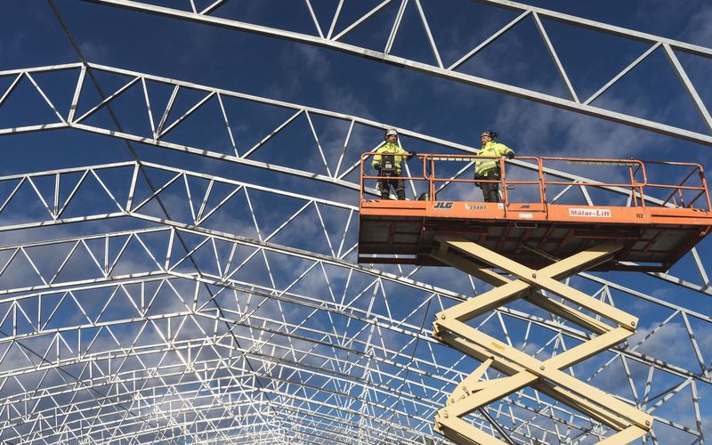 Scissor lift working at height under a steel roof frame (illustrative stock photo)